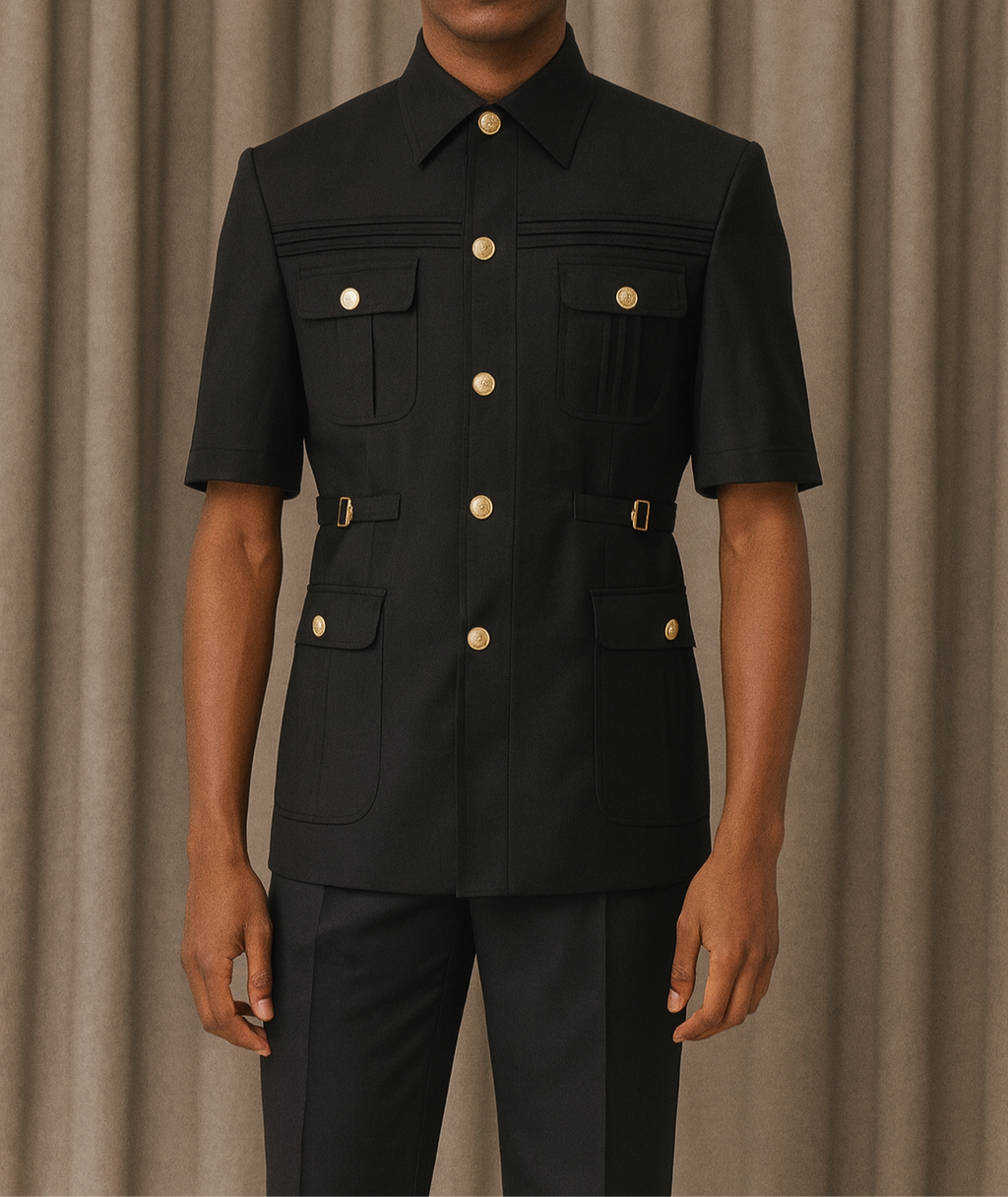 Man wearing a black outfit with gold buttons against a beige curtain background