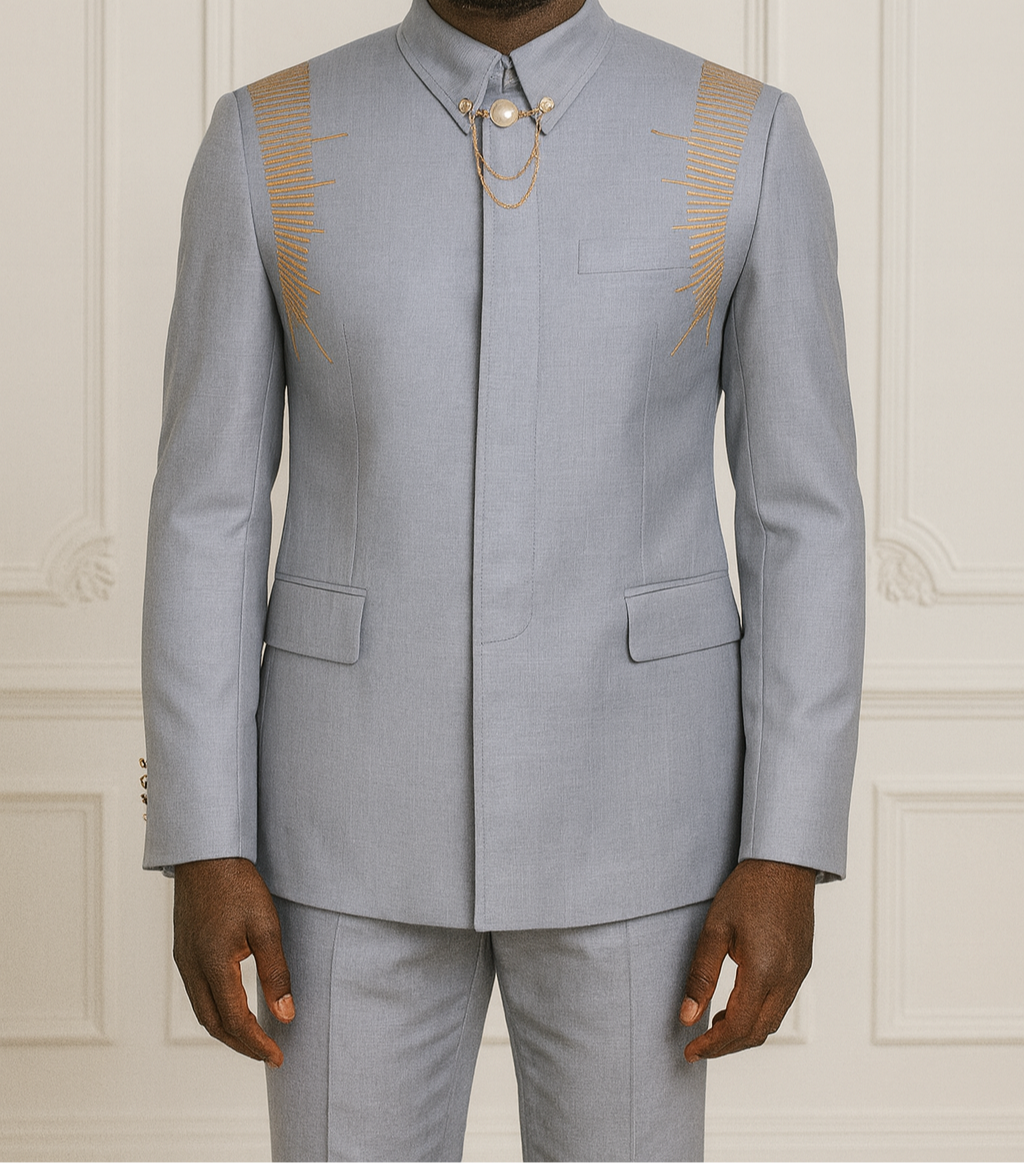 Man wearing a light gray suit with gold accents against a white paneled wall.