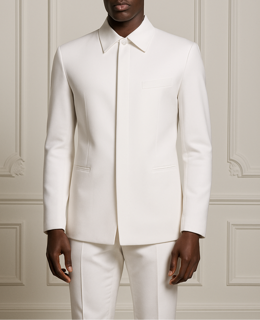 Man wearing a white suit standing against a light-colored paneled wall.
