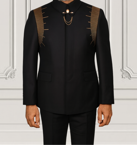 Man wearing a black traditional outfit with gold accents against a white wall.